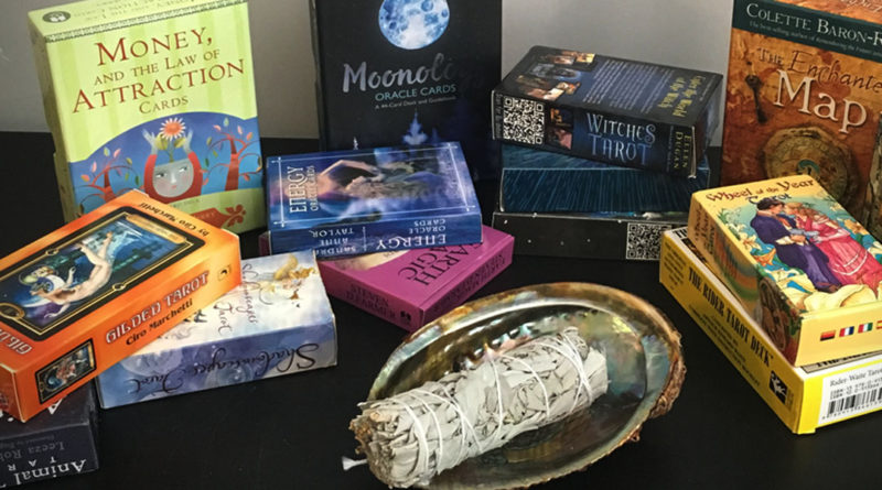 sage smudge stick in an abalone shell, surrounded by a collection tarot cards and oracle decks. When you bring home new tarot cards, you will want to cleanse your tarot cards to remove the energies from those who held them before you.